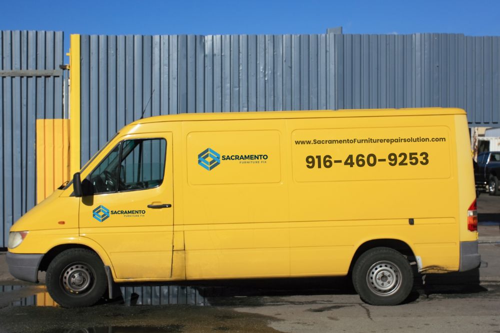 A bright yellow delivery van parked next to a corrugated metal wall, displaying its logo and phone number prominently.