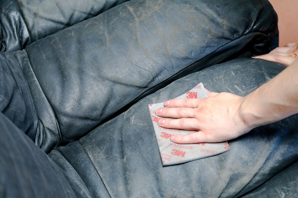 Individual cleaning a leather couch with a cloth, ensuring the surface is spotless and well-maintained.