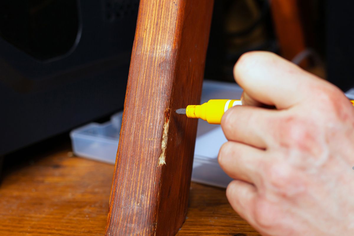 A person repairs a wooden chair's broken corners using a yellow marker to touch up damaged edges.