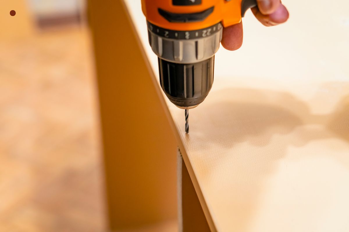 A person operates a drill to cut wood, assessing damage and gathering supplies for wood furniture repair.